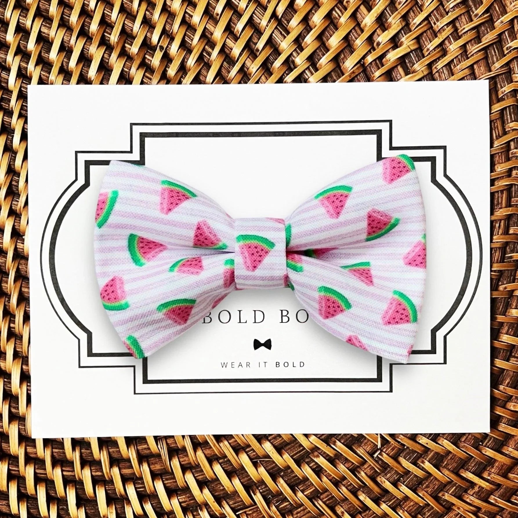 Pink watermelon patterned bow tie for pets displayed on a white card with a decorative border on a woven surface.
