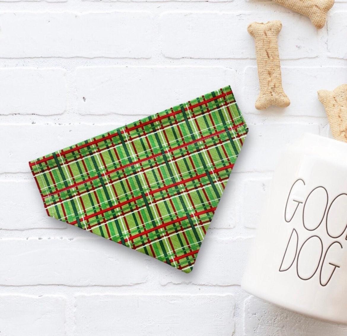 Green plaid Christmas dog bandana on a white surface with 'Good Dog' mug and dog bones.