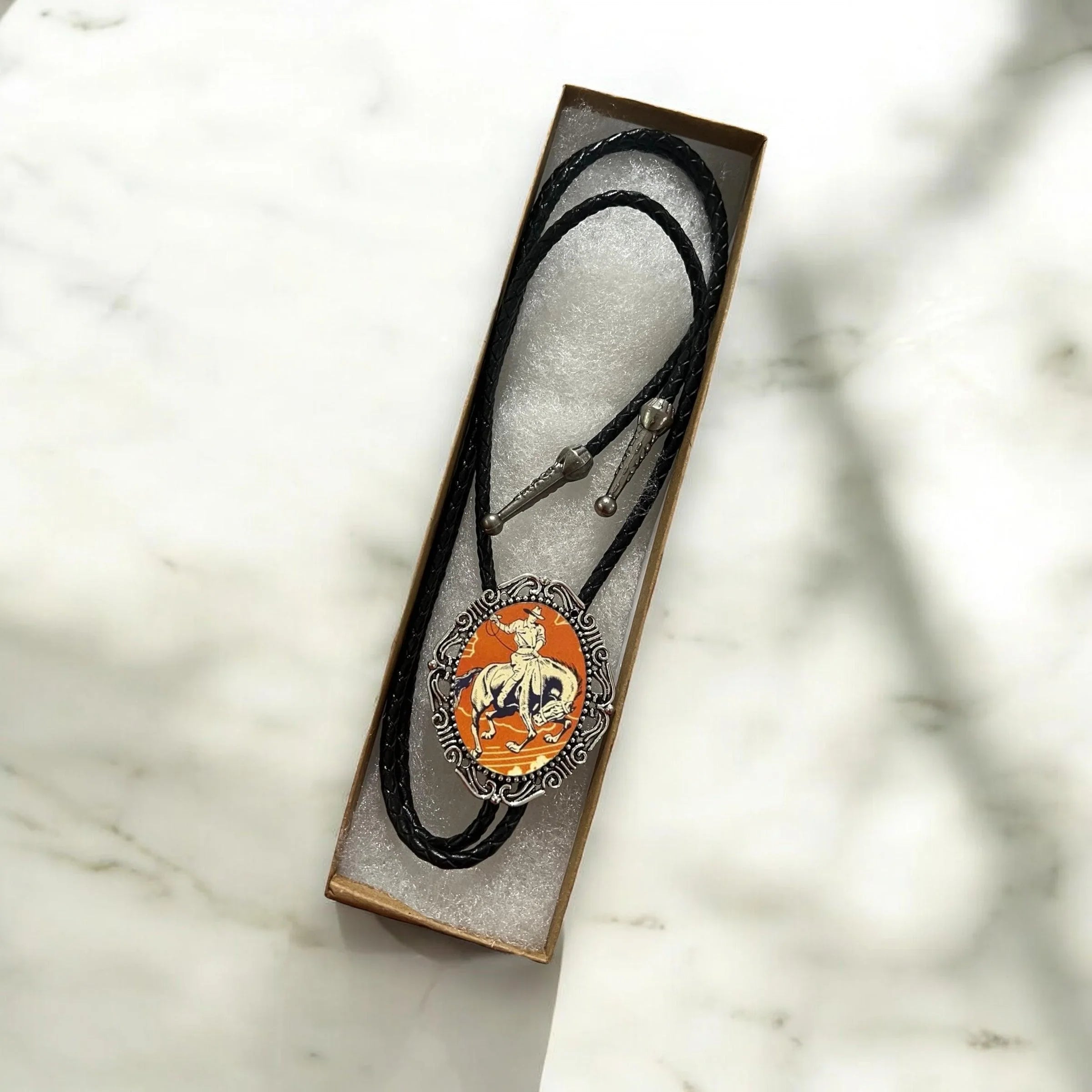 Orange cowboy silver bolo tie with black cord.
