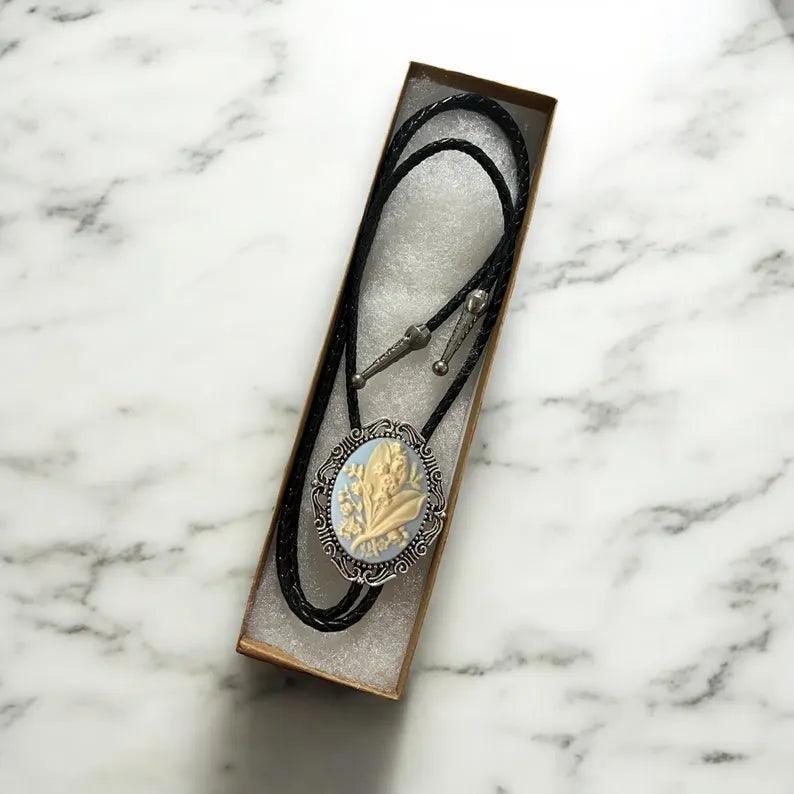 Blue and ivory Lily of the Valley bolo tie with ornate oval cameo in a display box.