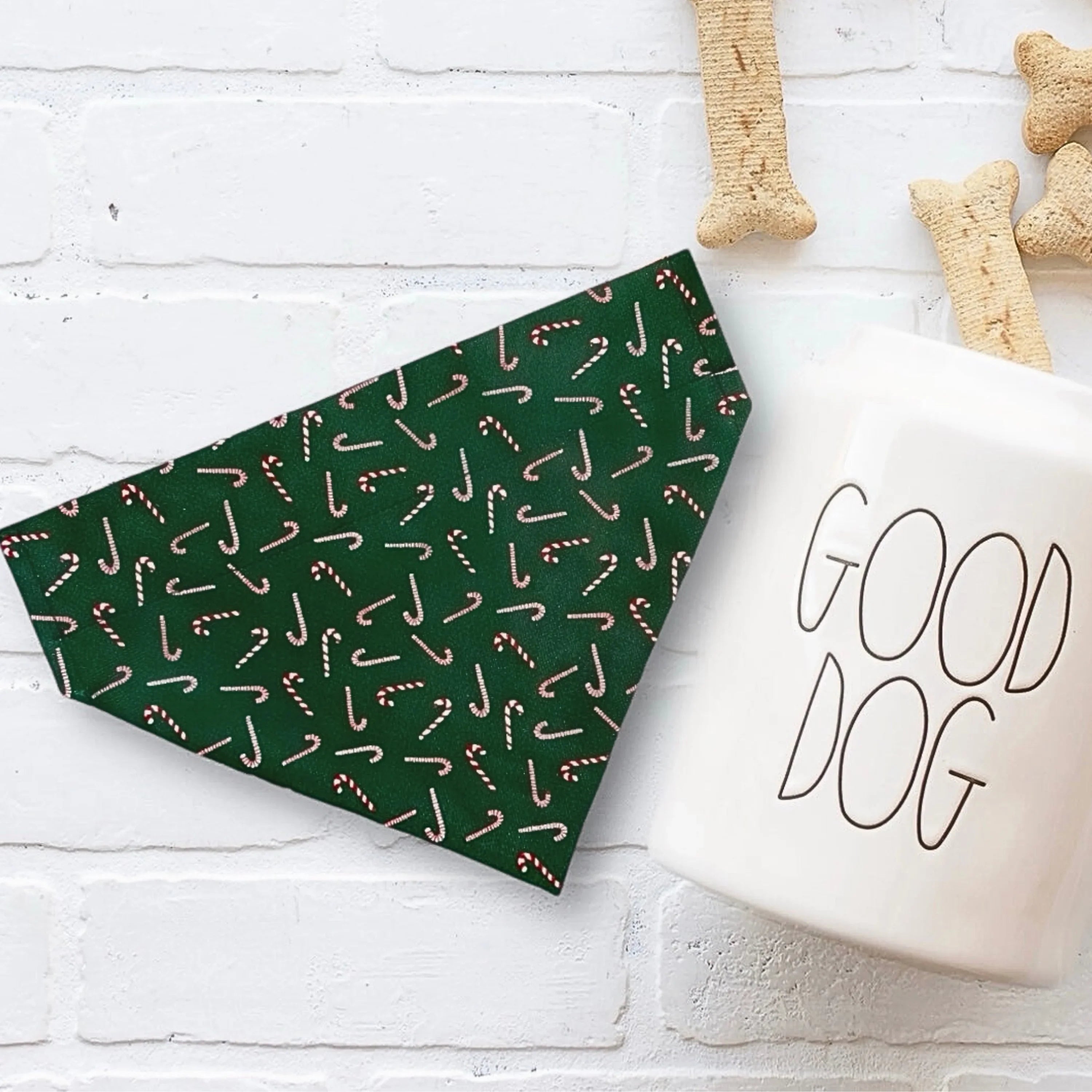 Green candy cane print dog bandana on a white surface with bone shaped chews