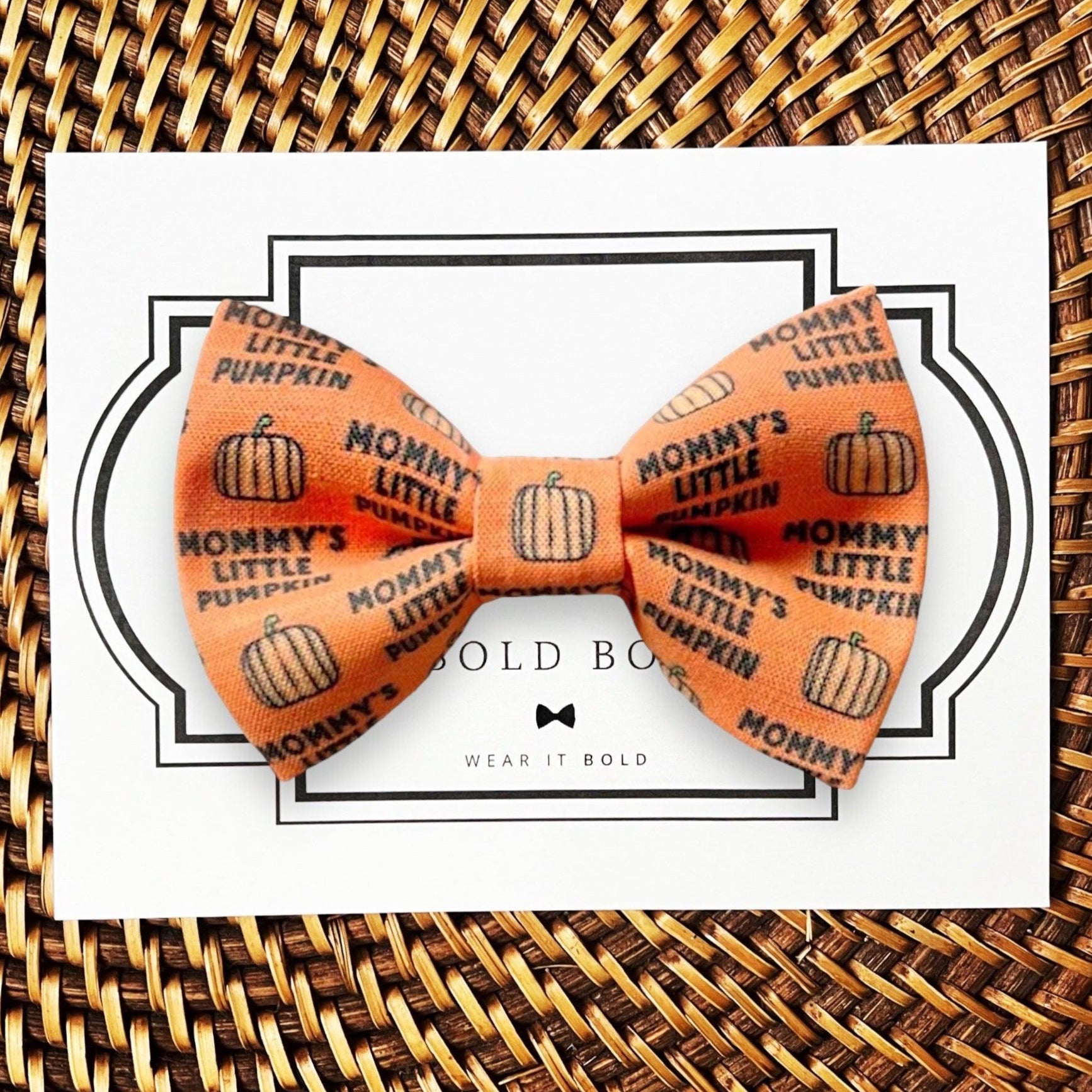 An orange dog bow tie that says "Mommy's little pumpkin" with pumpkin patterns, displayed on a card with the brand name 'The Bold Bow Tie'.