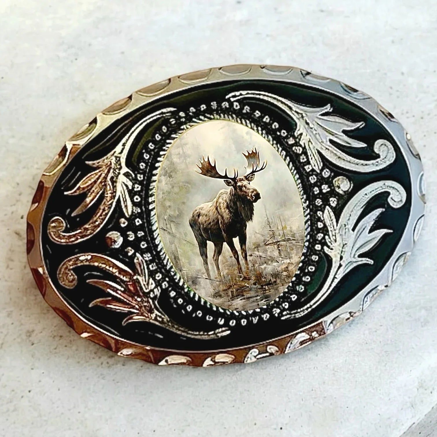 Decorative cowboy belt buckle with a moose motif surrounded by ornate black and gold scrollwork.