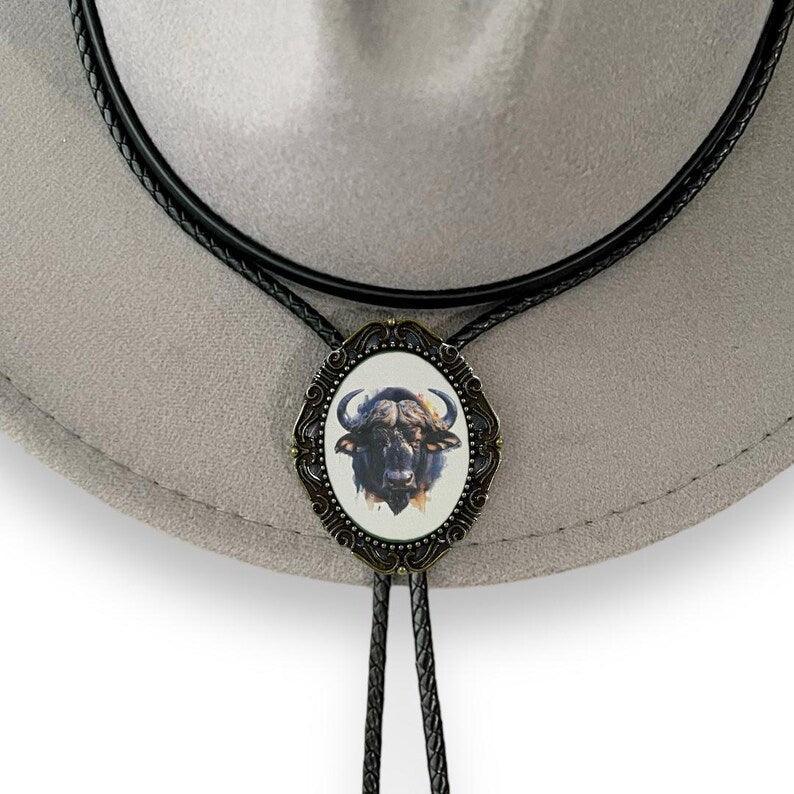 Vintage style bison bolo tie with an ornate frame and braided leather cords resting on a hat