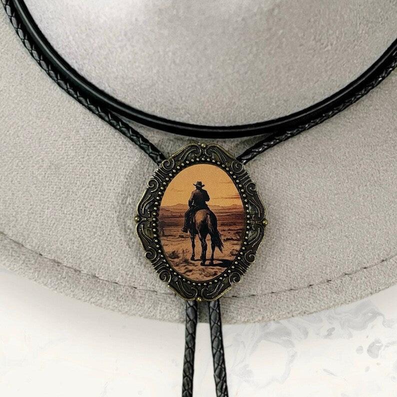 Sunset cowboy bolo tie showing a rider on horseback in a decorative frame against a desert sunset