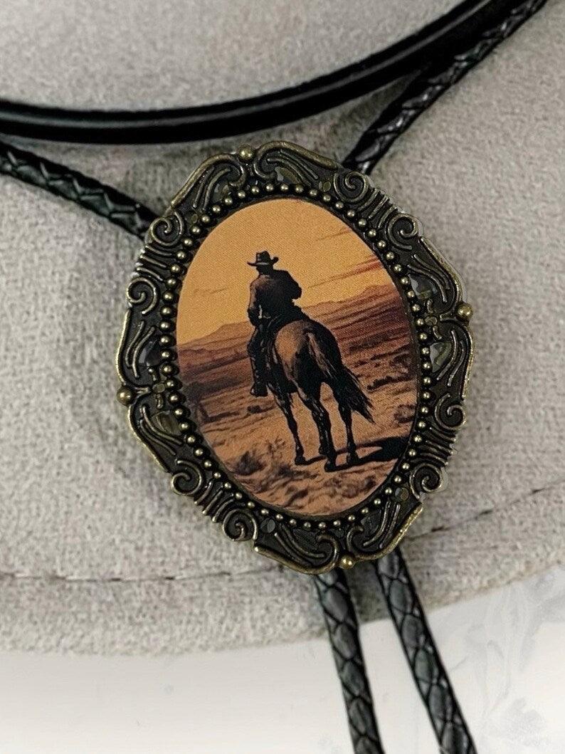 Sunset Cowboy Bolo Tie with ornate bronze frame surrounding an oval desert scene of a cowboy on horseback.