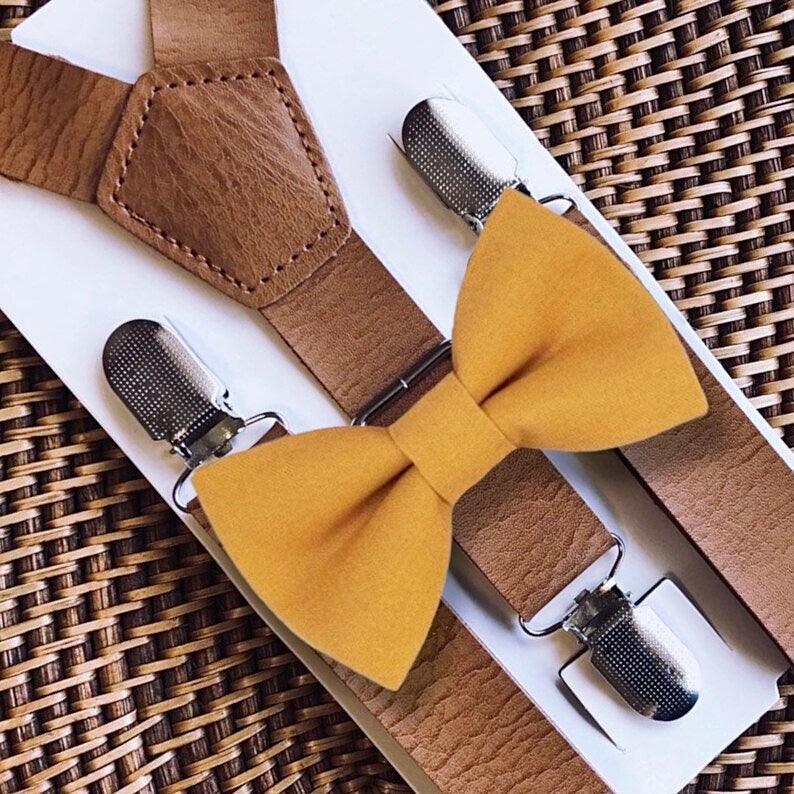 Brown suspenders with mustard yellow bow ties on a woven surface