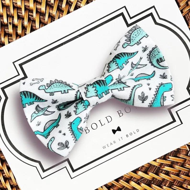 Blue dinosaur pattern bow tie for dog or cat collar displayed on a white packaging card