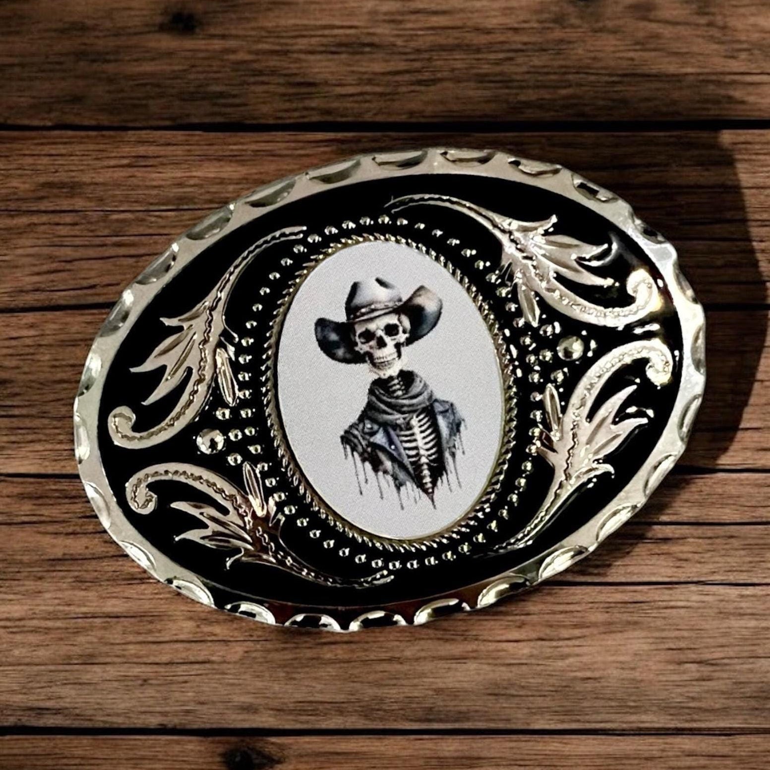 Decorative belt buckle with skeleton wearing a cowboy hat on a wooden surface