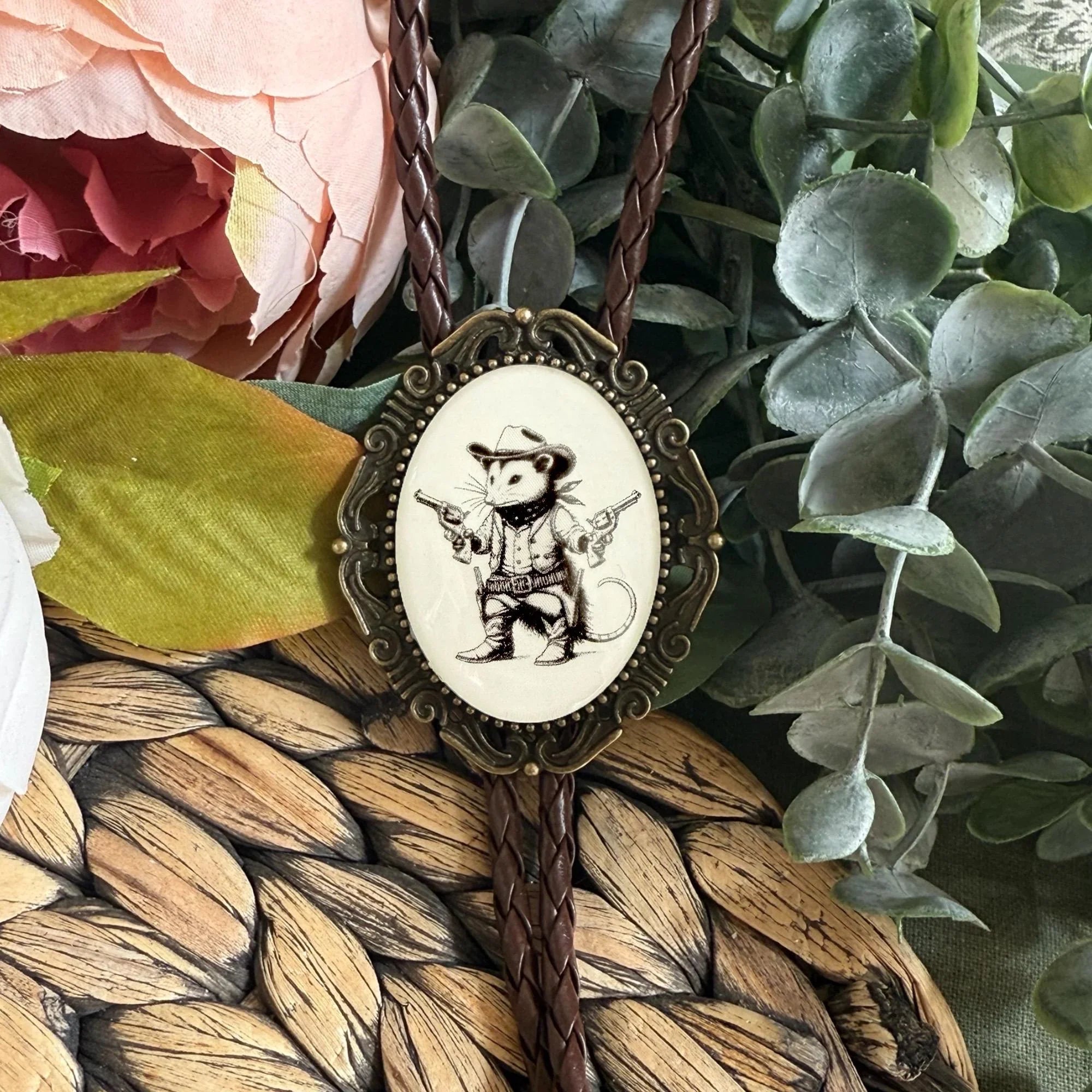 Vintage bolo tie with opossum on a table with flowers.