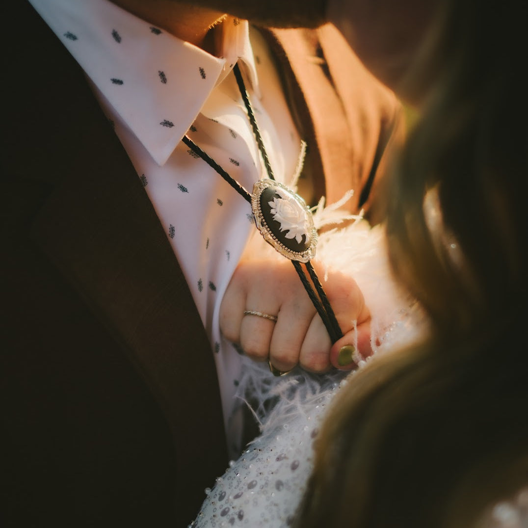 Close-up of a rose bolo tie worn by a person in a wedding.