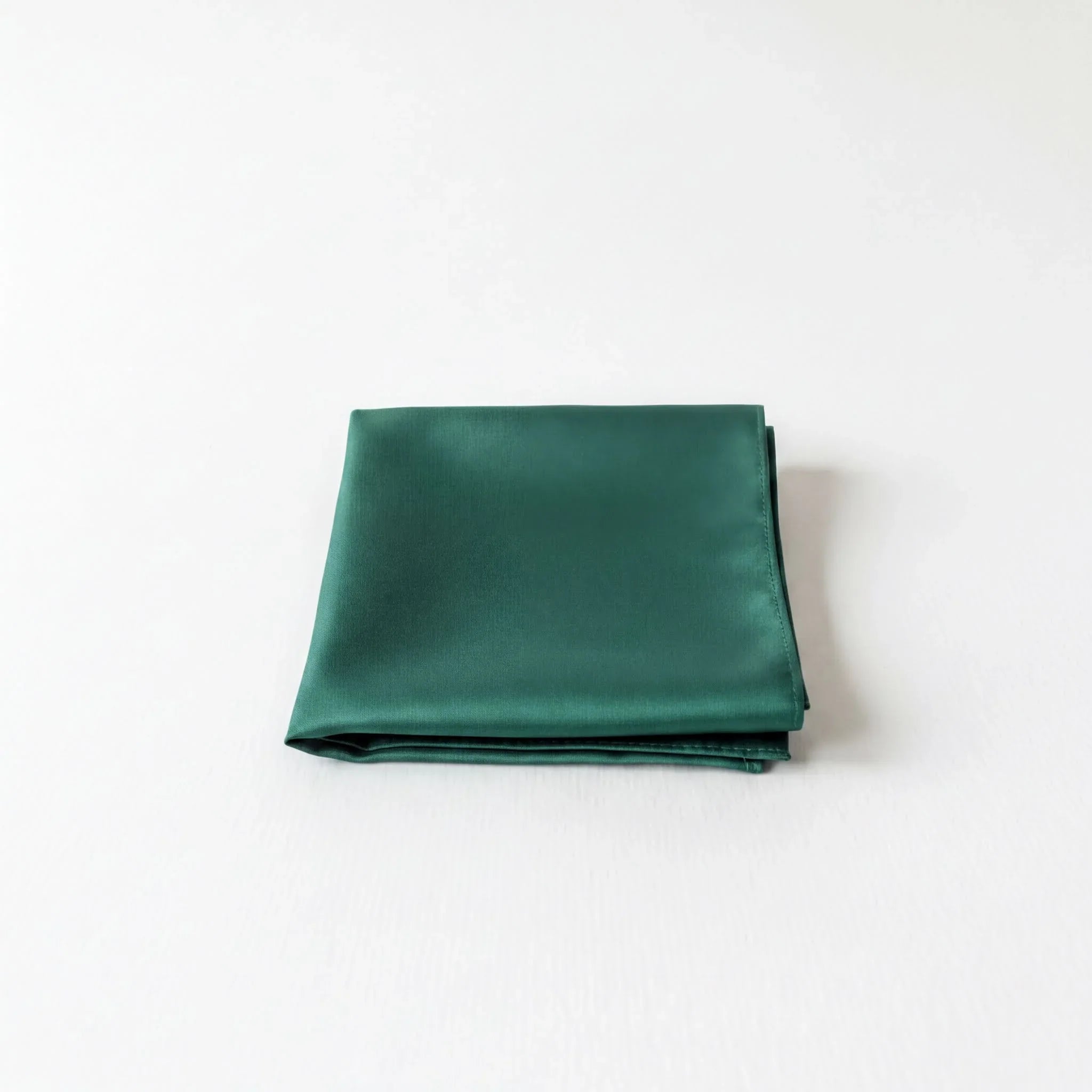 A dark green satin handkerchief is neatly folded and placed on a white surface.