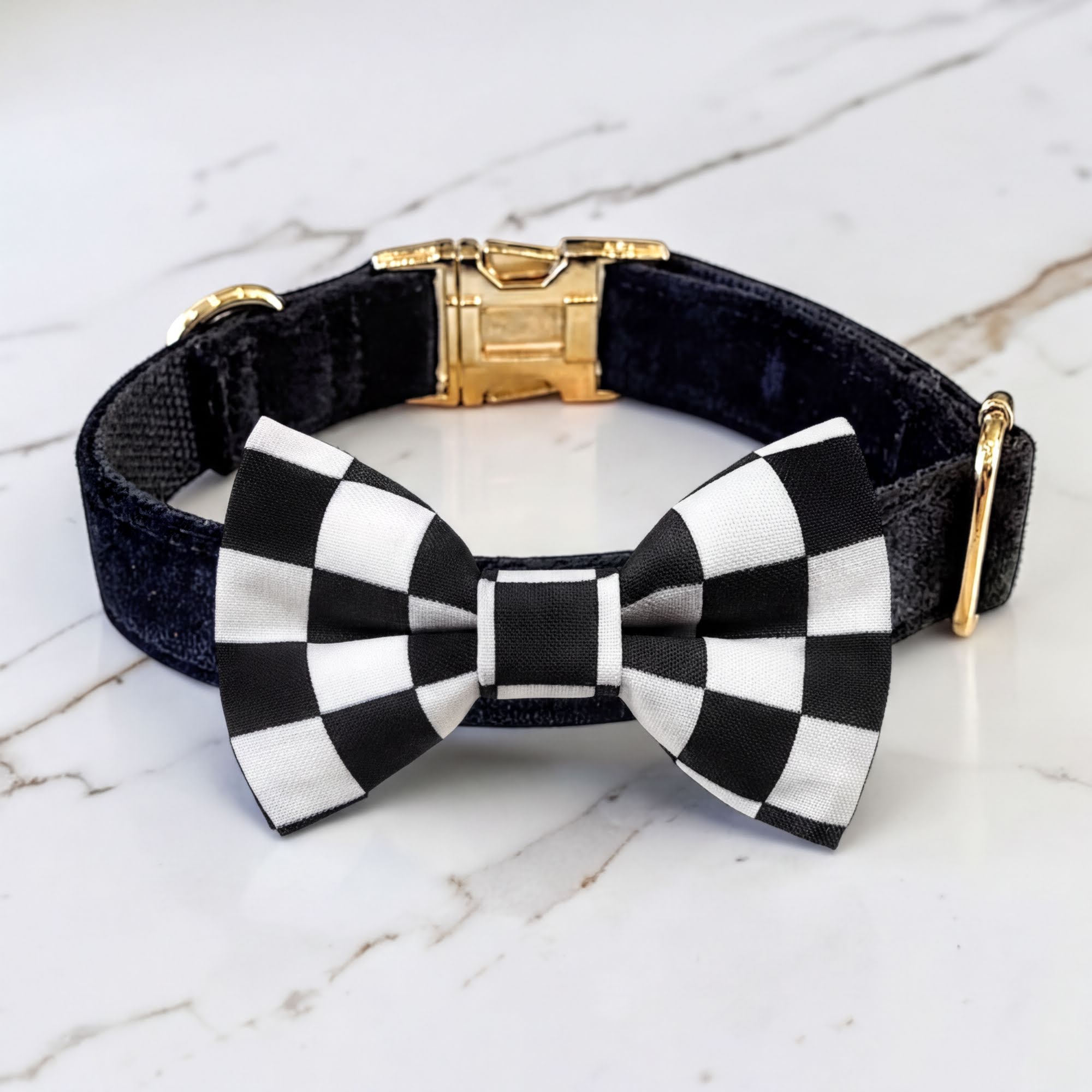 Black velvet dog collar with black and white checkered pt bowtie a gold clasp on a marble surface.