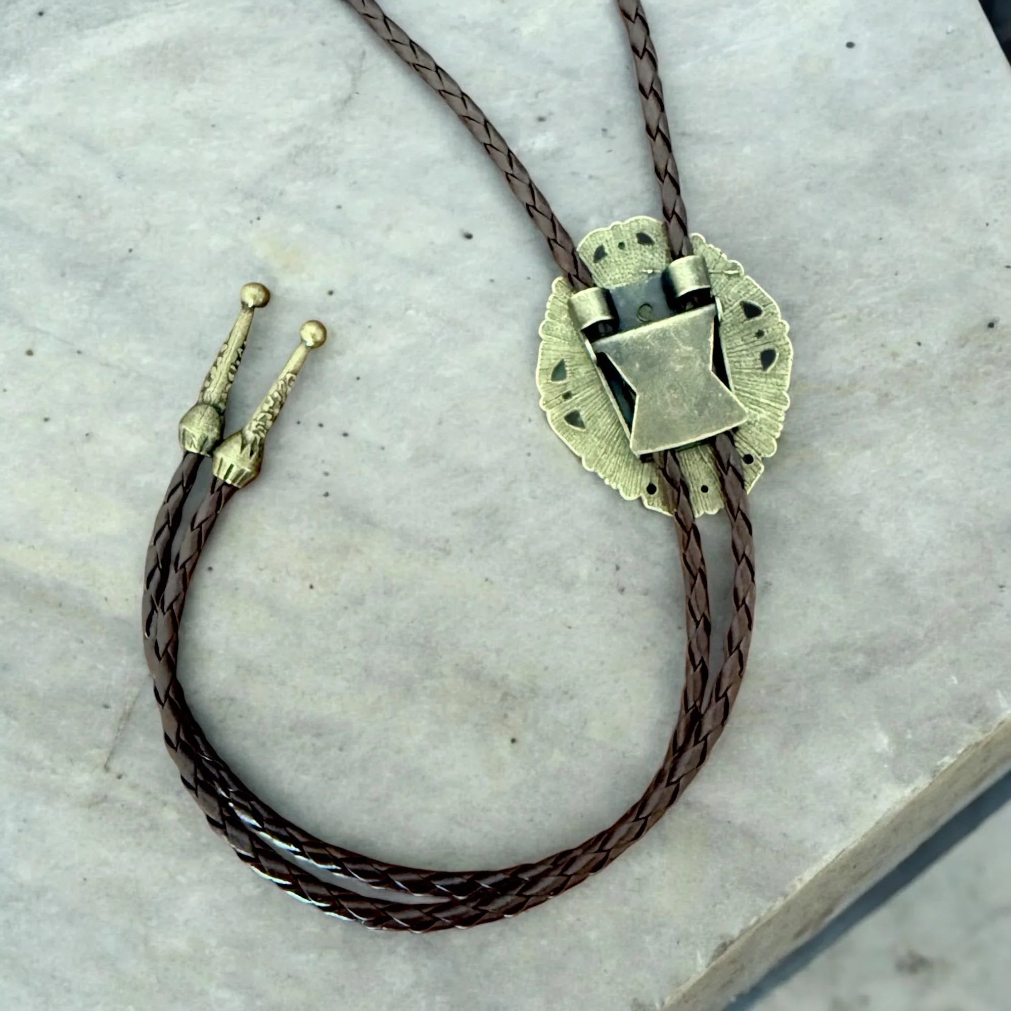 Bolo tie with bronze clasp on a marble surface