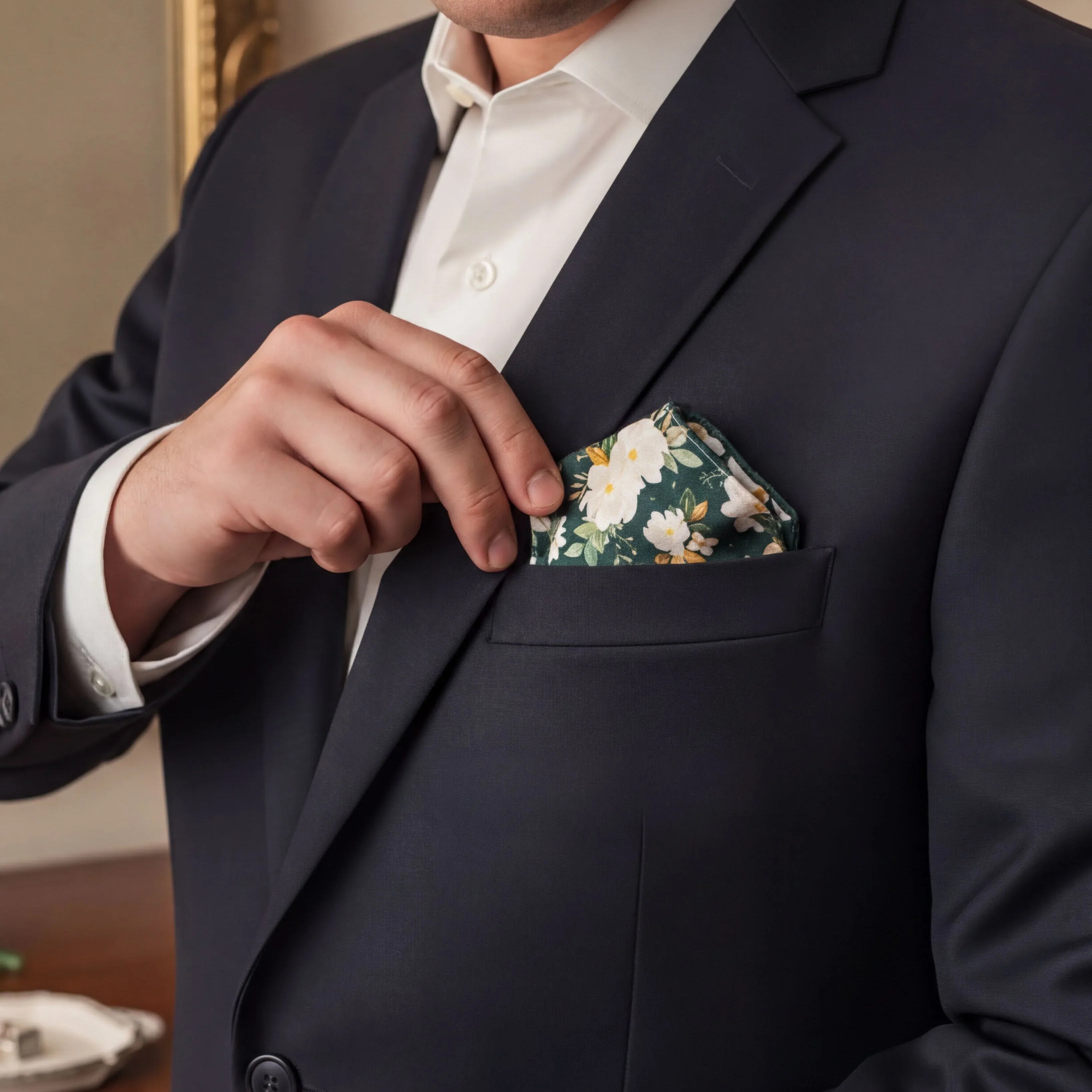 A groomsman in a dark suit jacket is holding a pocket square with a floral pattern.