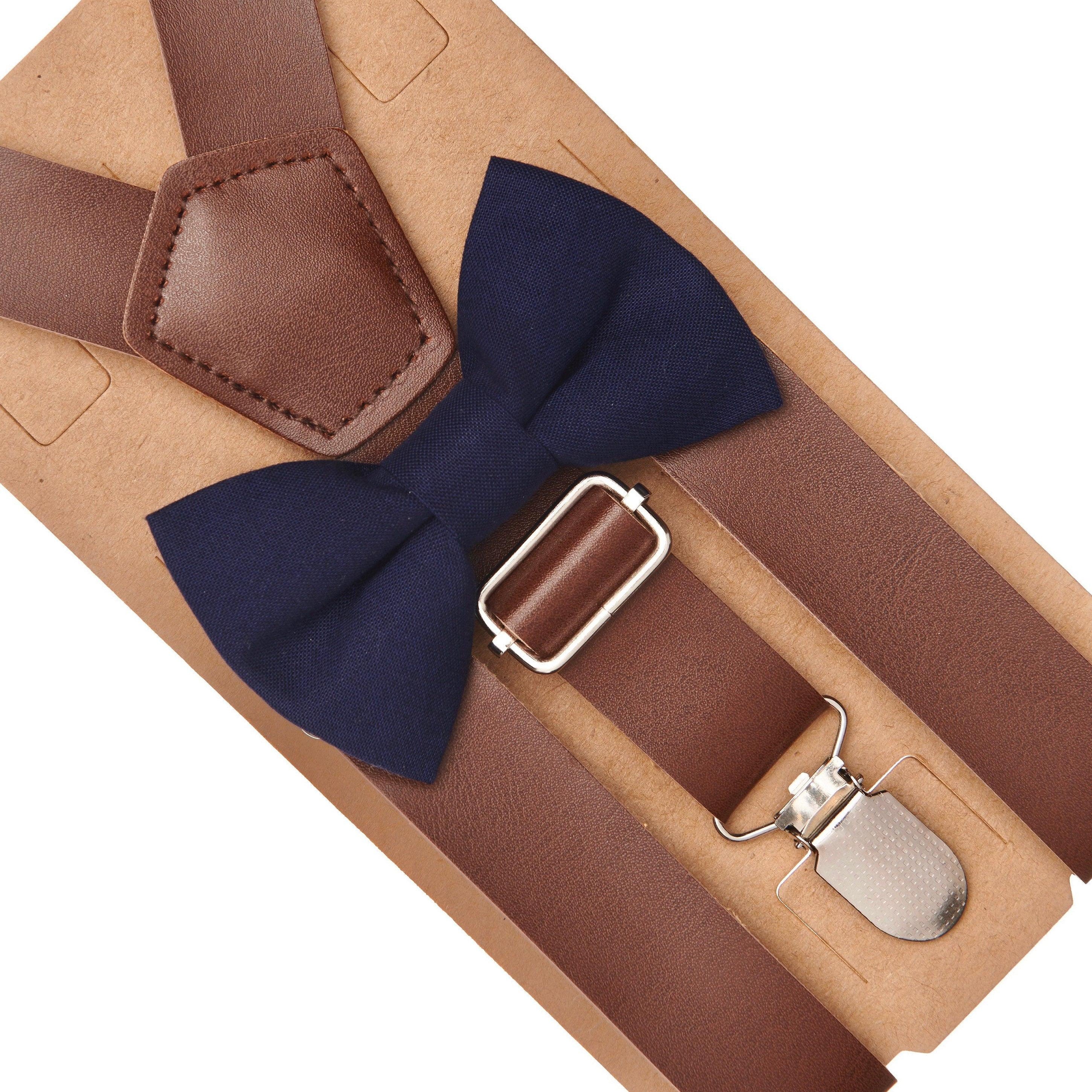 Brown suspenders with a navy bow tie and silver clip on a beige background