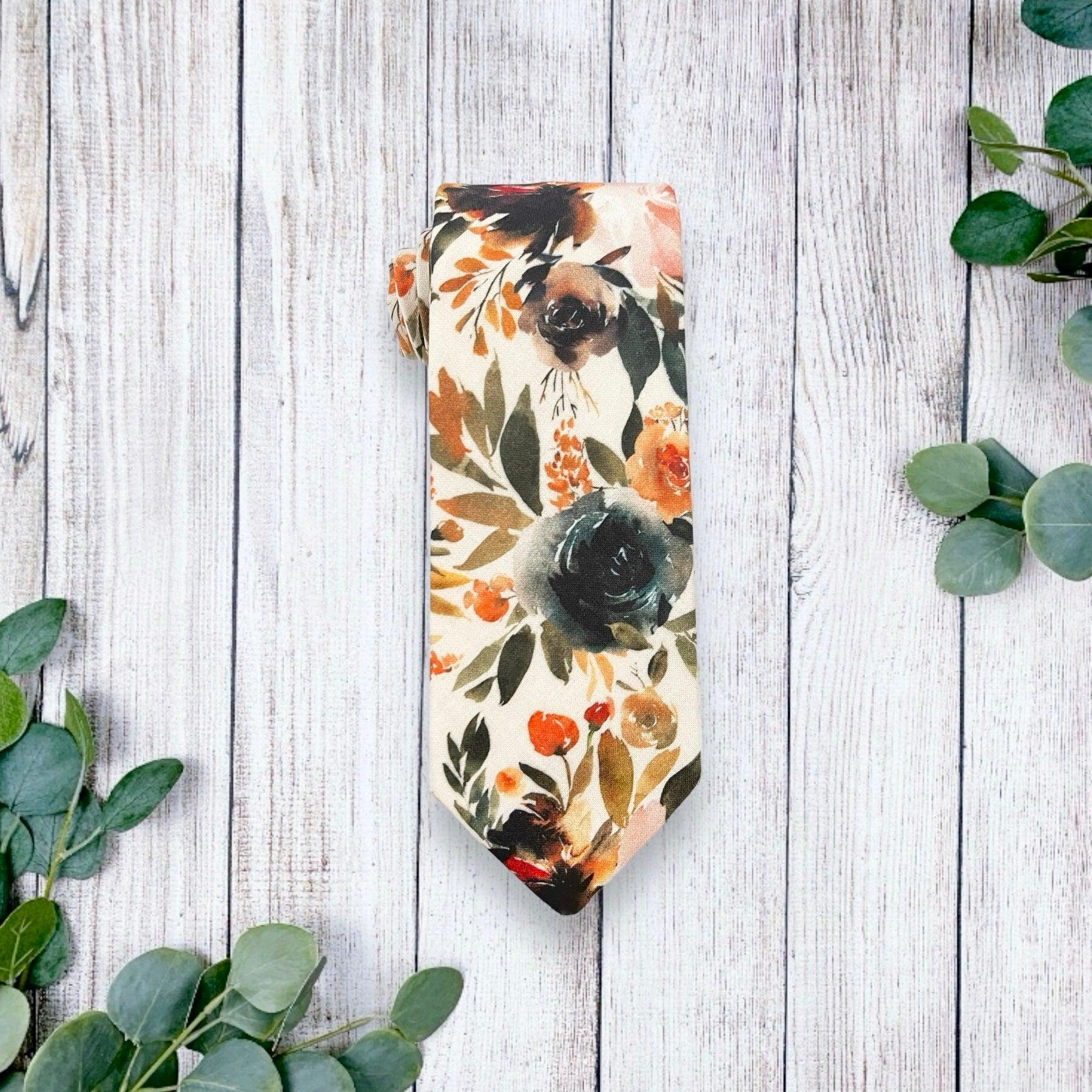 Floral patterned tie on a light wooden surface with eucalyptus leaves around