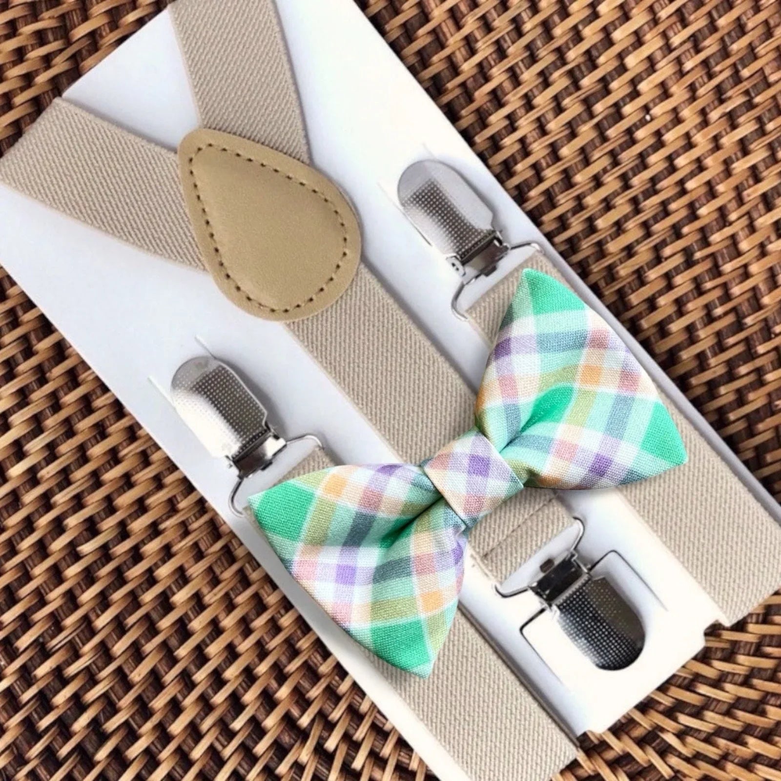Set of plaid bow ties and suspenders in a box on a woven surface