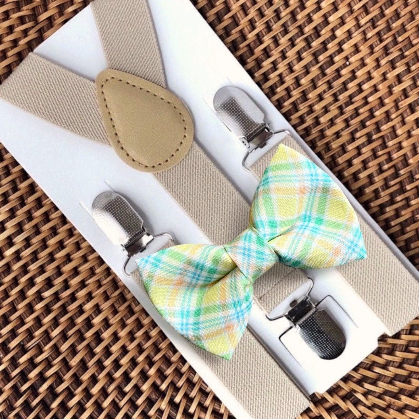 Pastel plaid bow tie with tan suspenders displayed on a white card against a woven surface