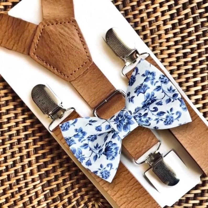 Brown suspenders with blue floral bow ties on a woven surface