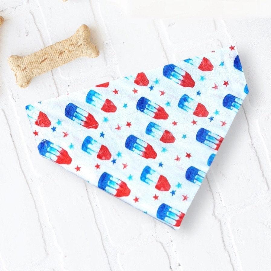 Folded white pet bandana with red blue bomb pop pattern on a light background