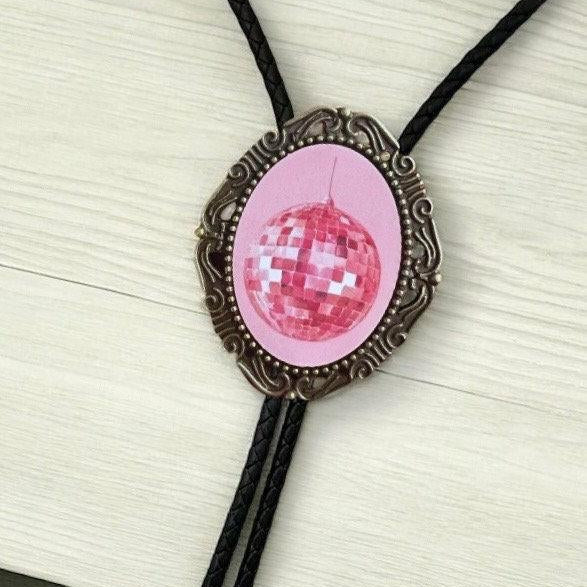 Pink disco ball pendant in a bronze ornate frame with a black braided bolo cord close up