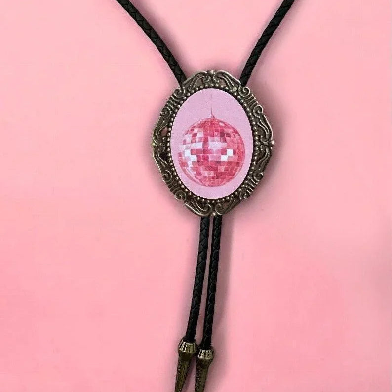 Close up of pink disco ball bolo pendant in a decorative bronze frame against a pink backdrop