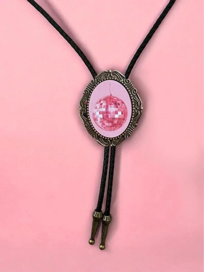 Close up of pink disco ball bolo pendant in a decorative bronze frame against a pink backdrop