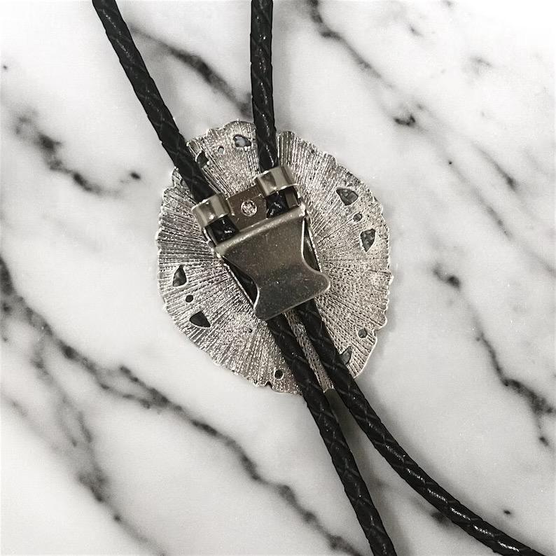 Silver tips for a bolo tie shown on black leather cord next to a green plant