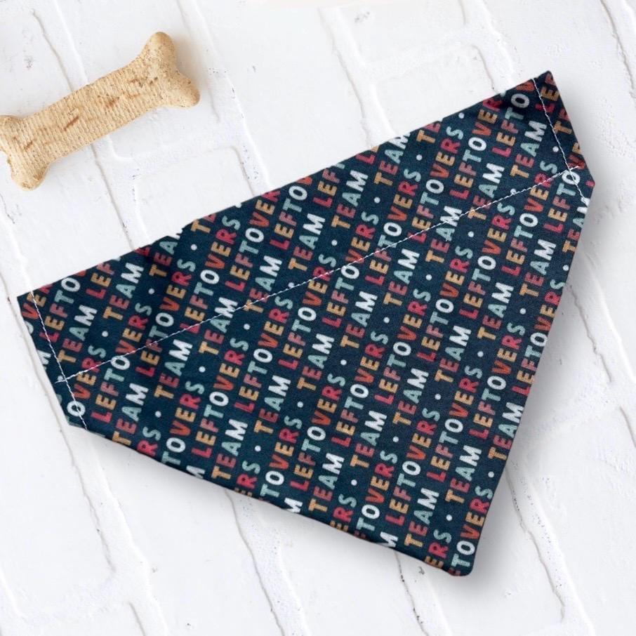 Navy Thanksgiving dog bandana with colorful Team Leftovers print laid on a white surface