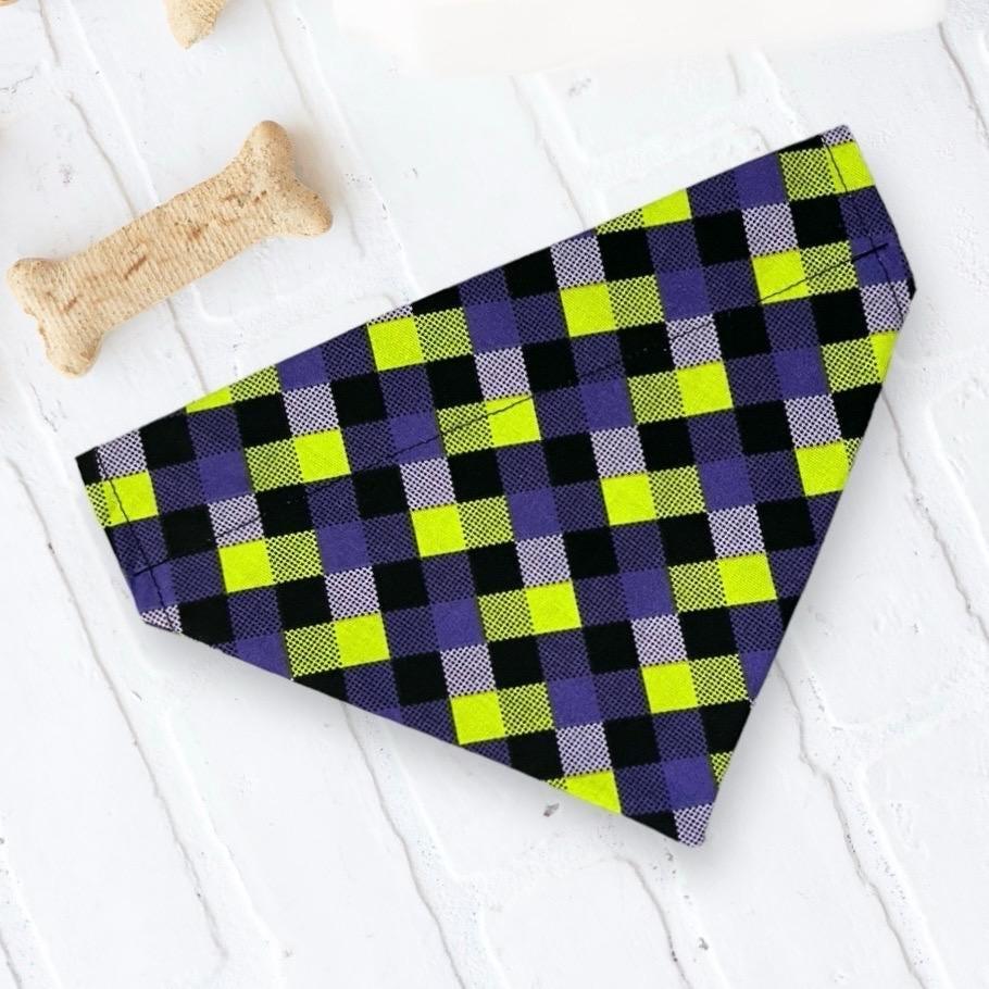 Purple, lime, and black plaid dog bandana laid flat with a bone nearby.