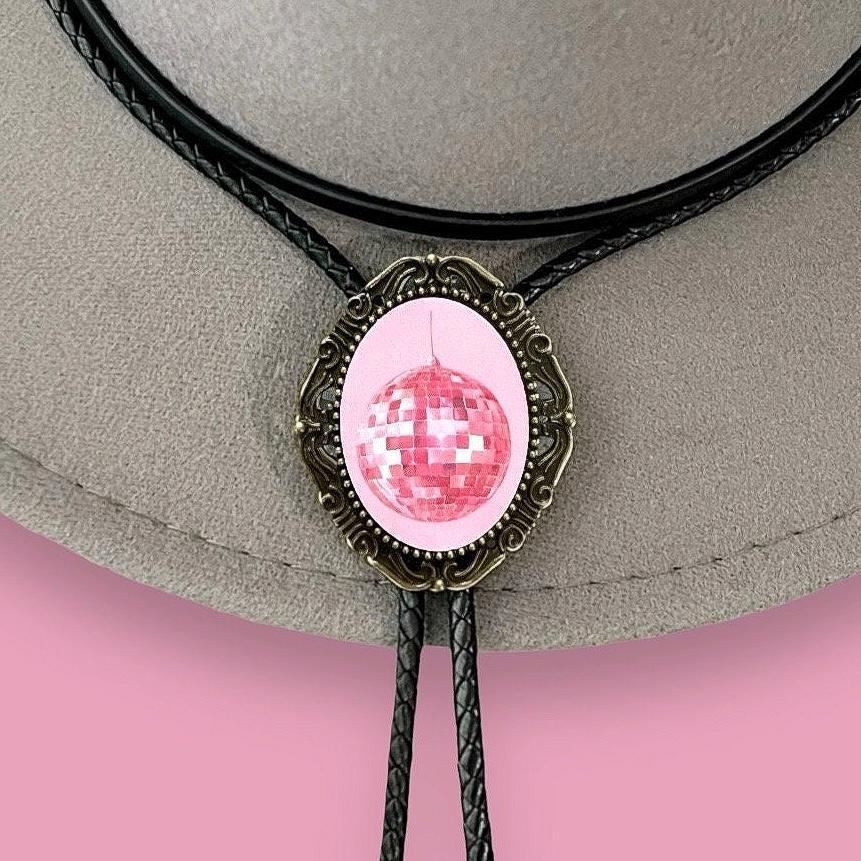 Pink disco ball bolo pendant set in an ornate bronze frame on a gray surface