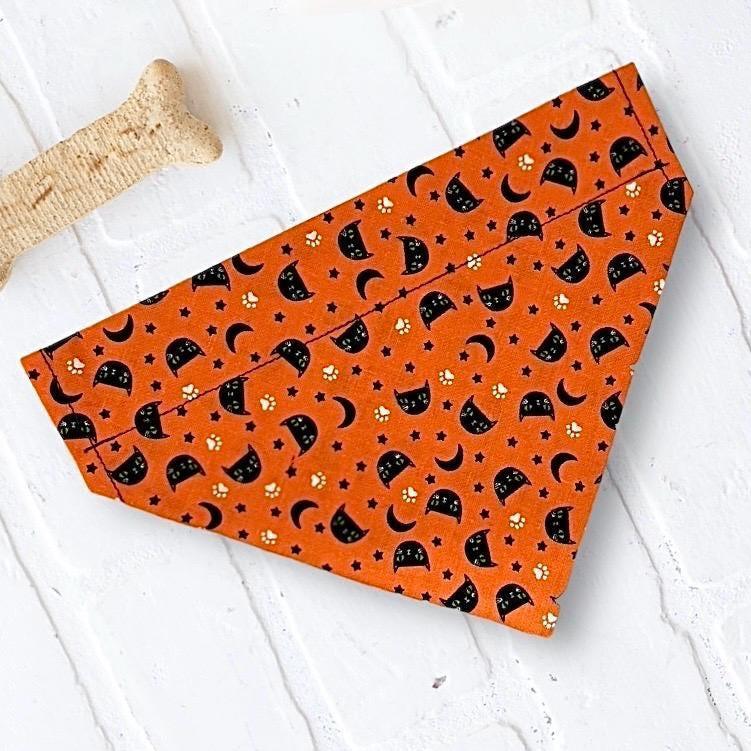 Orange Halloween bandana with black cat faces and crescent moons laid flat on a white surface