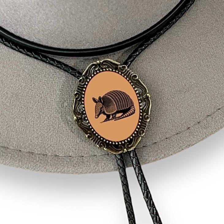 Close up of bolo tie slide with an armadillo emblem on an orange oval in an ornate metal setting