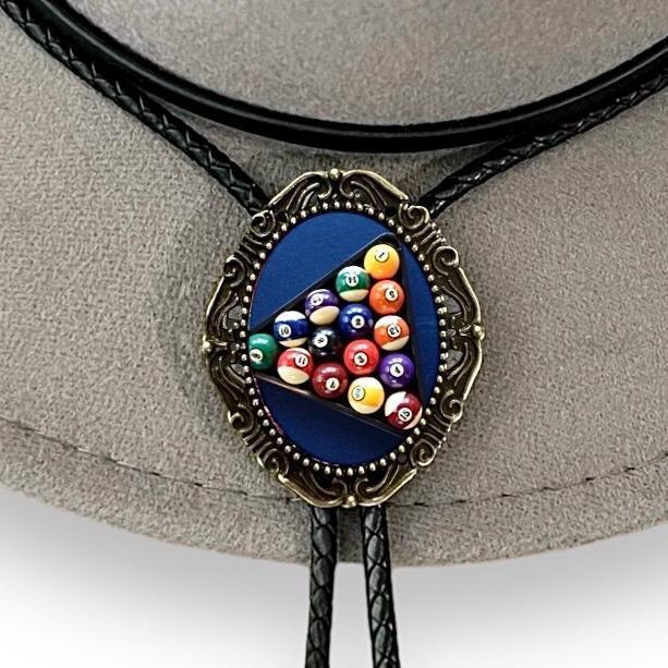 Infographic from The Bold Bow Tie titled Bolo Tie Features. Right: A vintage-style bolo tie with a blue and white cowboy riding a horse illustration inside an ornate bronze filigree frame on a black braided cord. Left: Lines connect the image to three checkmark features: Handmade, 39" Long Cord, and Pendant is 1.5" (L) x 1.25" (W). Bottom text reads Perfect Addition to Your Outfit.