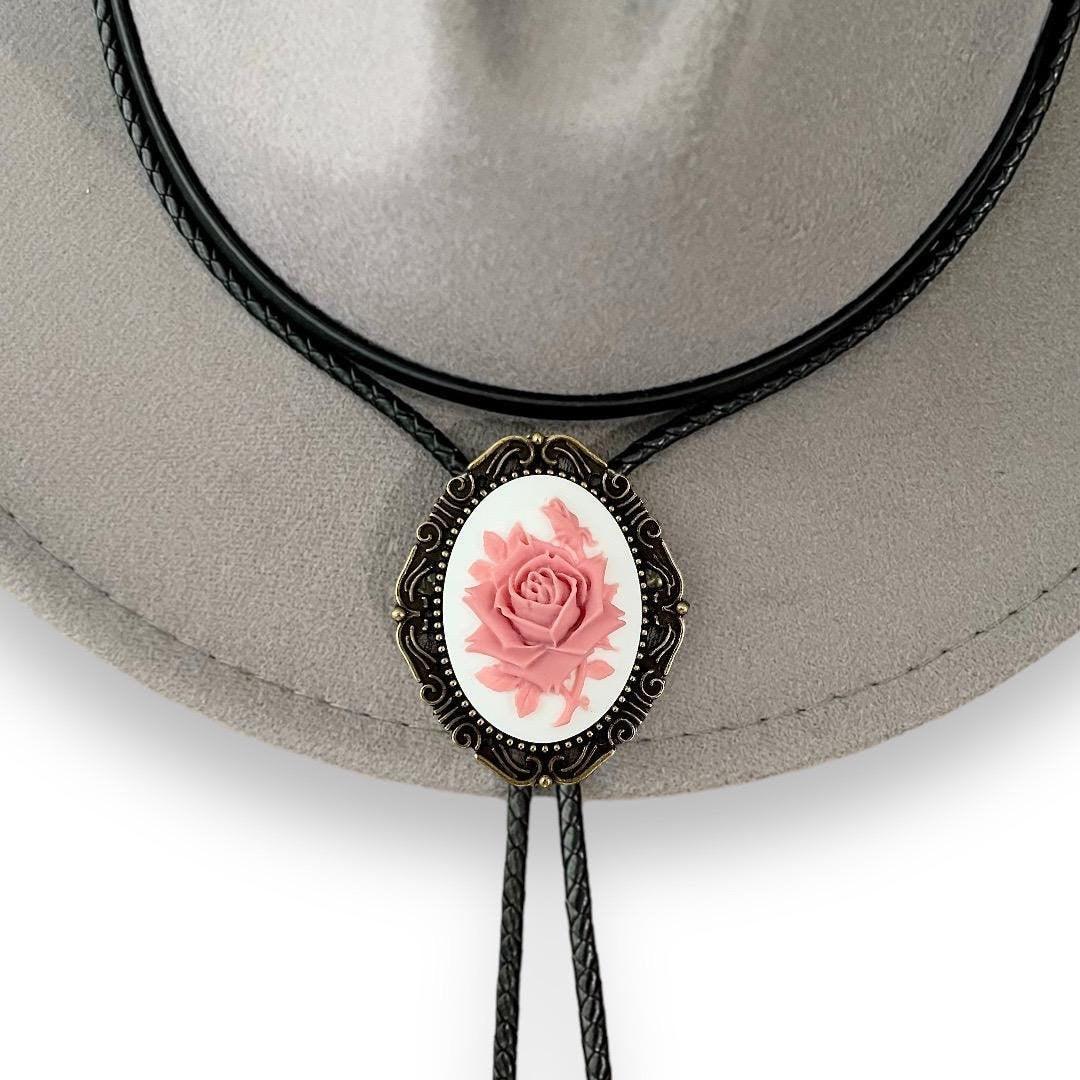 Infographic from The Bold Bow Tie titled Bolo Tie Features. Right: A vintage-style bolo tie with a blue and white cowboy riding a horse illustration inside an ornate bronze filigree frame on a black braided cord. Left: Lines connect the image to three checkmark features: Handmade, 39" Long Cord, and Pendant is 1.5" (L) x 1.25" (W). Bottom text reads Perfect Addition to Your Outfit.