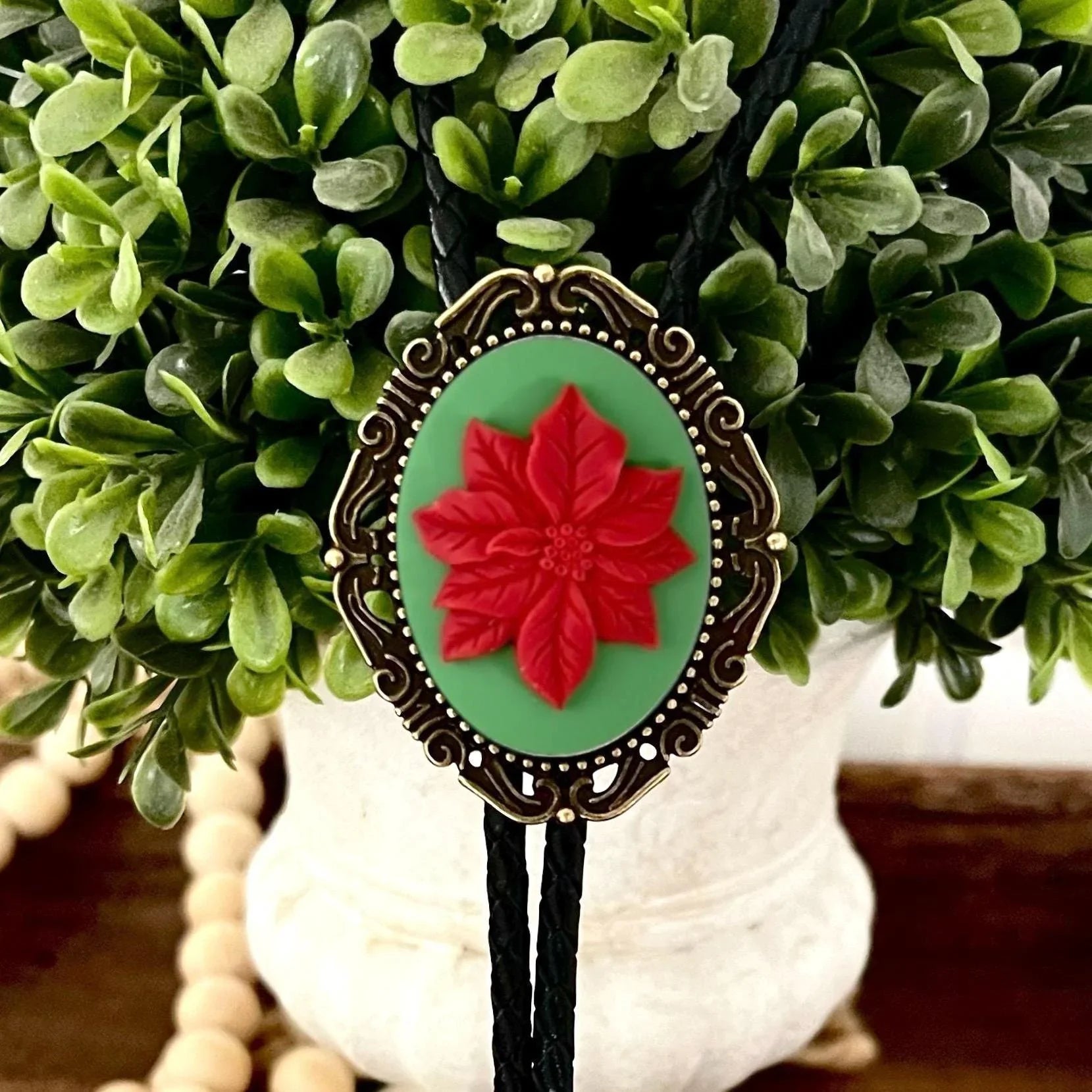 Bolo tie size chart from The Bold Bow Tie. The image displays a braided leather bolo tie with a round silver concho-style slide and silver metal tips, set against a multi-colored striped fabric background. A vertical dotted arrow on the right spans the full length of the piece, accompanied by text indicating a 39 inch cord length.