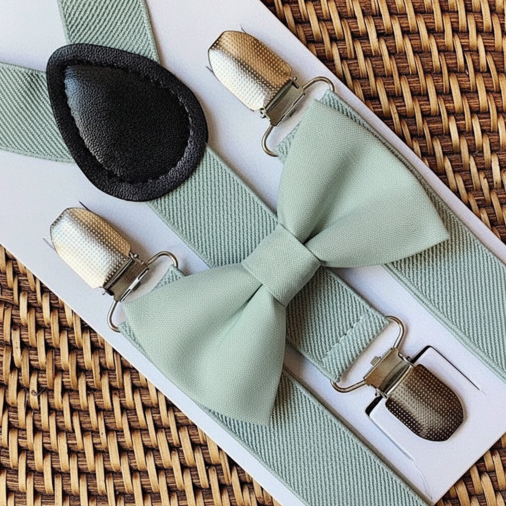 Sage green bowtie and suspenders for a wedding on a woven surface.