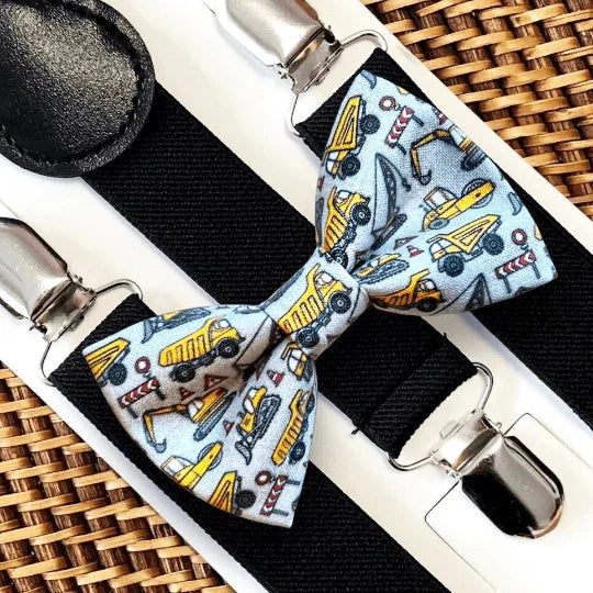 Toddler Bow tie with construction vehicle pattern on a black strap with silver clips, on a woven surface.