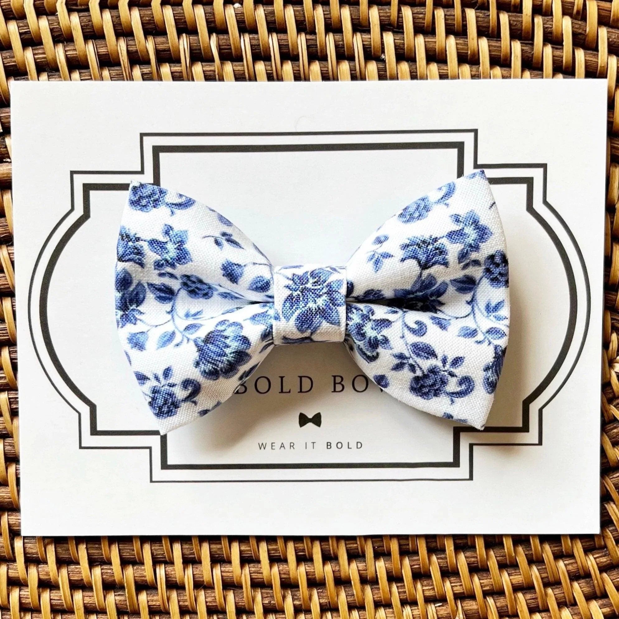 Blue floral bow tie close up on white packaging with a black framed border