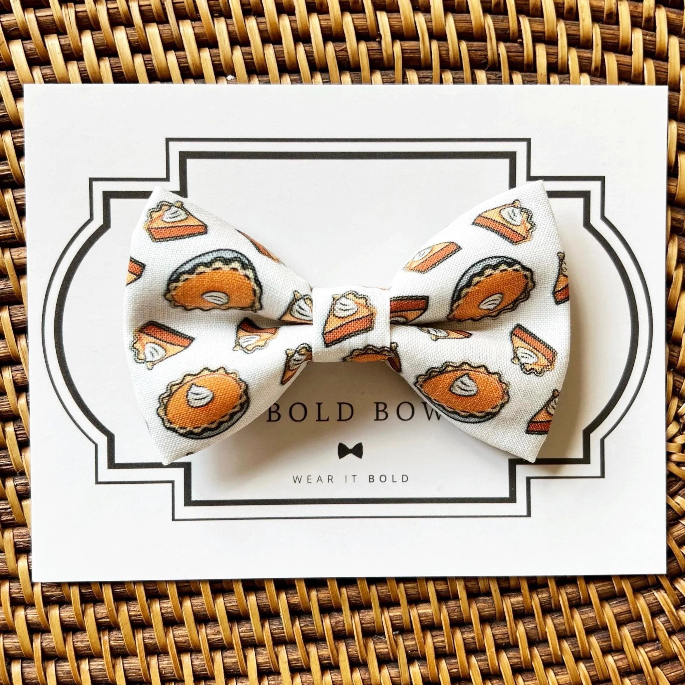 Thanksgiving themed pet bow tie with orange turkey print on pale fabric placed over a white gift card with a bold black border