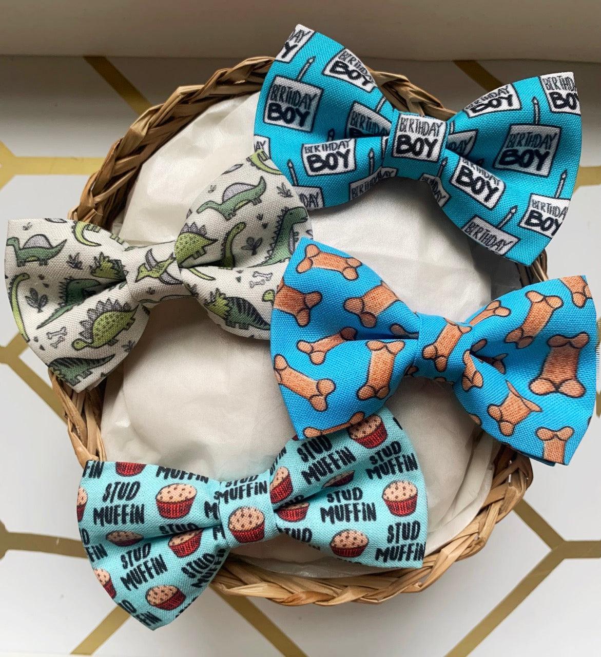 Gift set of three pet bow ties in blue birthday boy print pale dinosaur print and muffin print arranged in a wicker basket