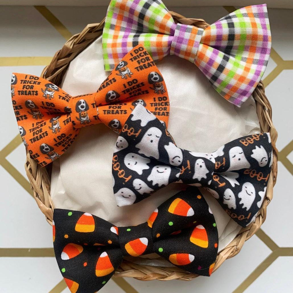 Halloween bow ties with ghost and candy corn patterns displayed in a basket on a wood surface