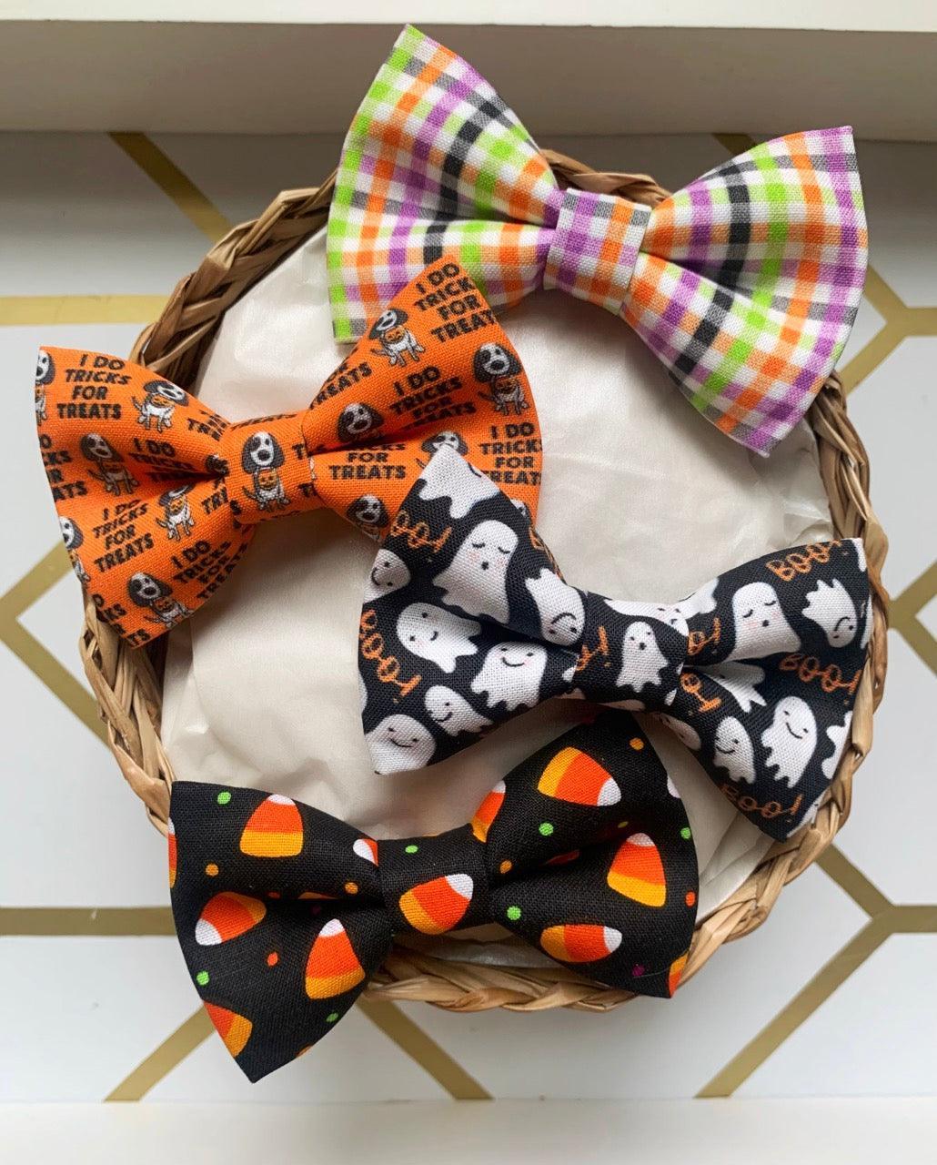 Halloween bow ties with ghost and candy corn patterns displayed in a basket on a wood surface
