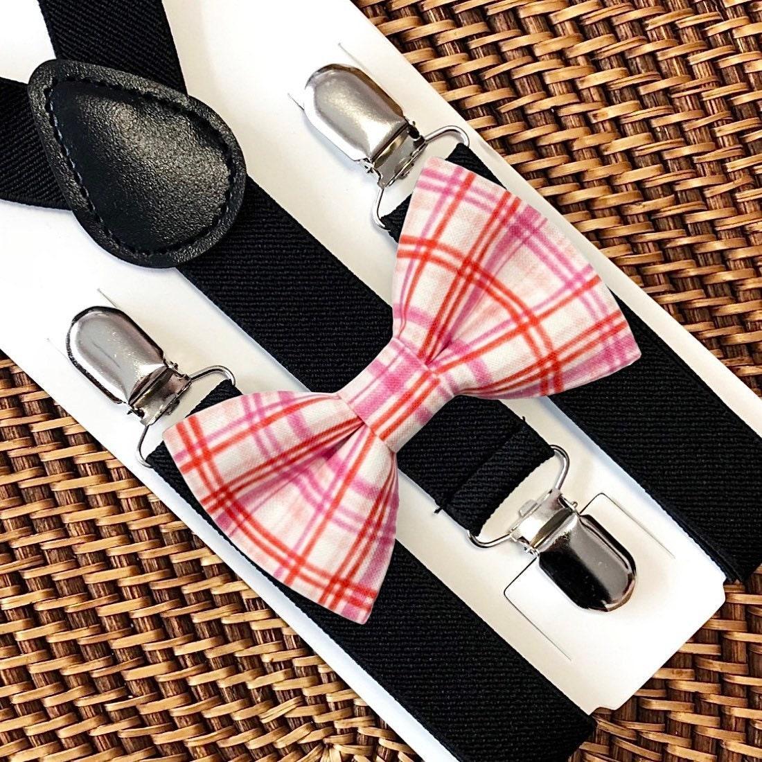 Plaid bow tie with reds and pinks with black suspenders on a woven surface