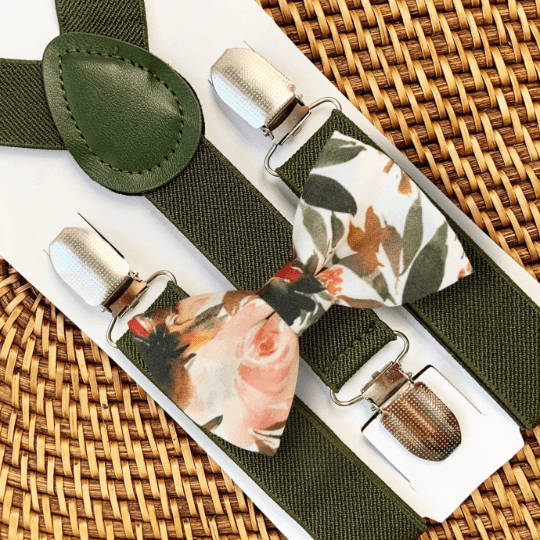 A set of olive green elastic suspenders with a floral bow tie on a woven background.