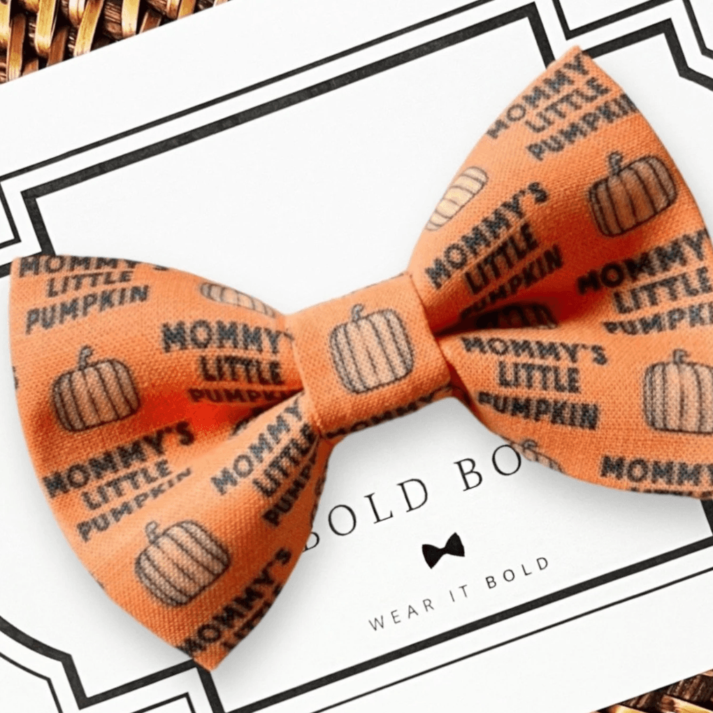 An orange dog bow tie that says "Mommy's little pumpkin" with pumpkin patterns, displayed on a card with the brand name 'The Bold Bow Tie'.