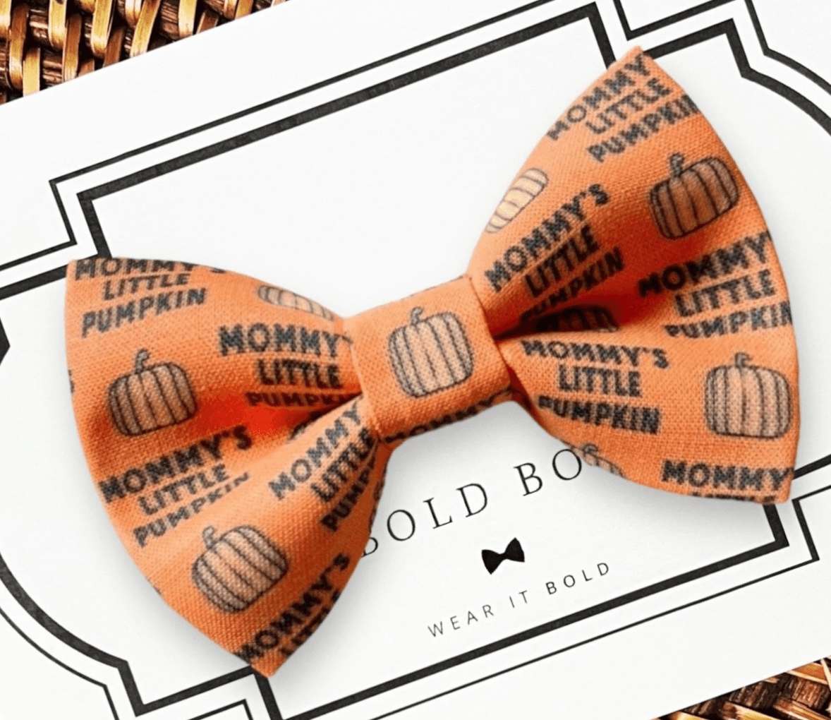 An orange dog bow tie that says "Mommy's little pumpkin" with pumpkin patterns, displayed on a card with the brand name 'The Bold Bow Tie'.