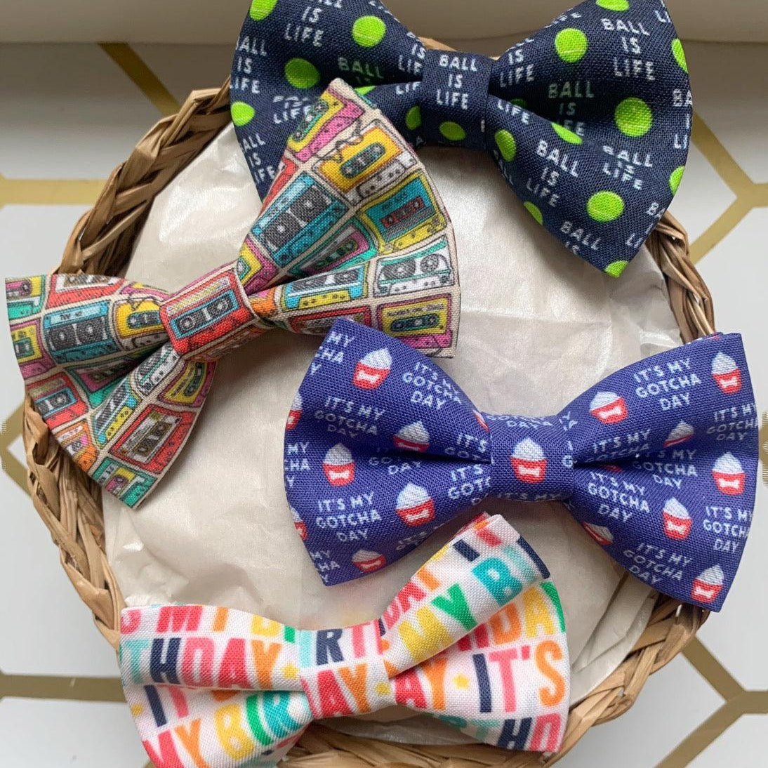 Basket with four colorful bow ties in playful patterns for pets including cassette tape and birthday text designs