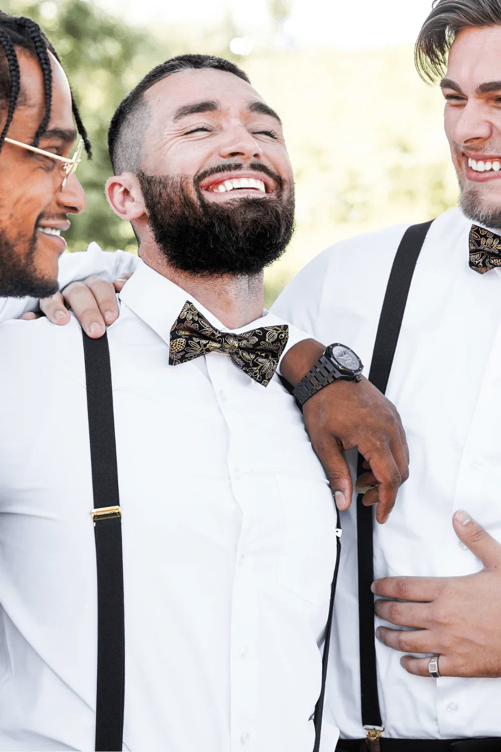 Groomsmen at a wedding wearing black and gold bow ties and black suspenders with gold clips.